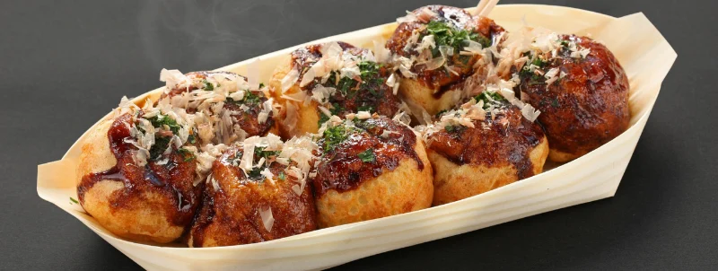 舟皿に盛られた、かつお節をかけた焼きたてのたこ焼き