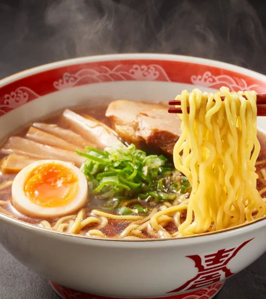 赤い丼に盛られた、煮卵とチャーシューを添えた醤油ラーメン